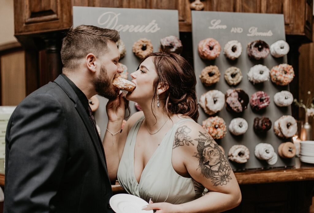 Couple each taking a bite of a donut on both sides.