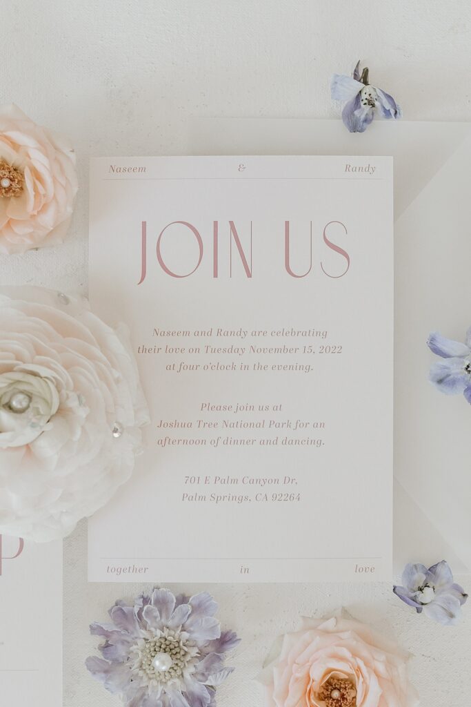 Wedding invitation in white with pink writing on flat lay image