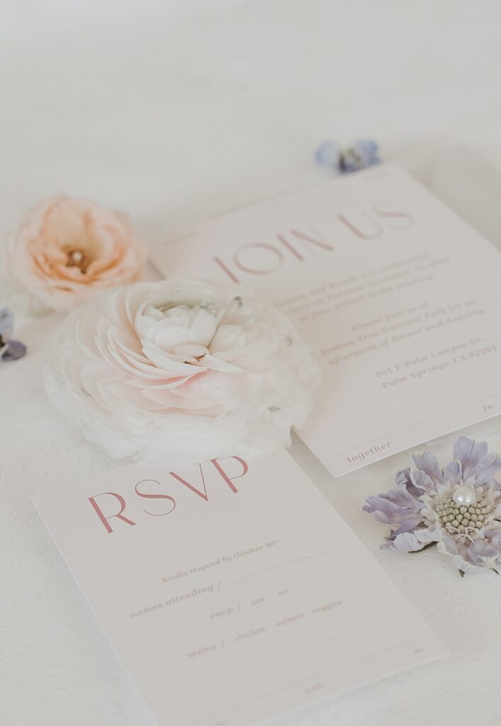 White, orange, and purple florals with wedding invitation and RSVP on flat lay photo