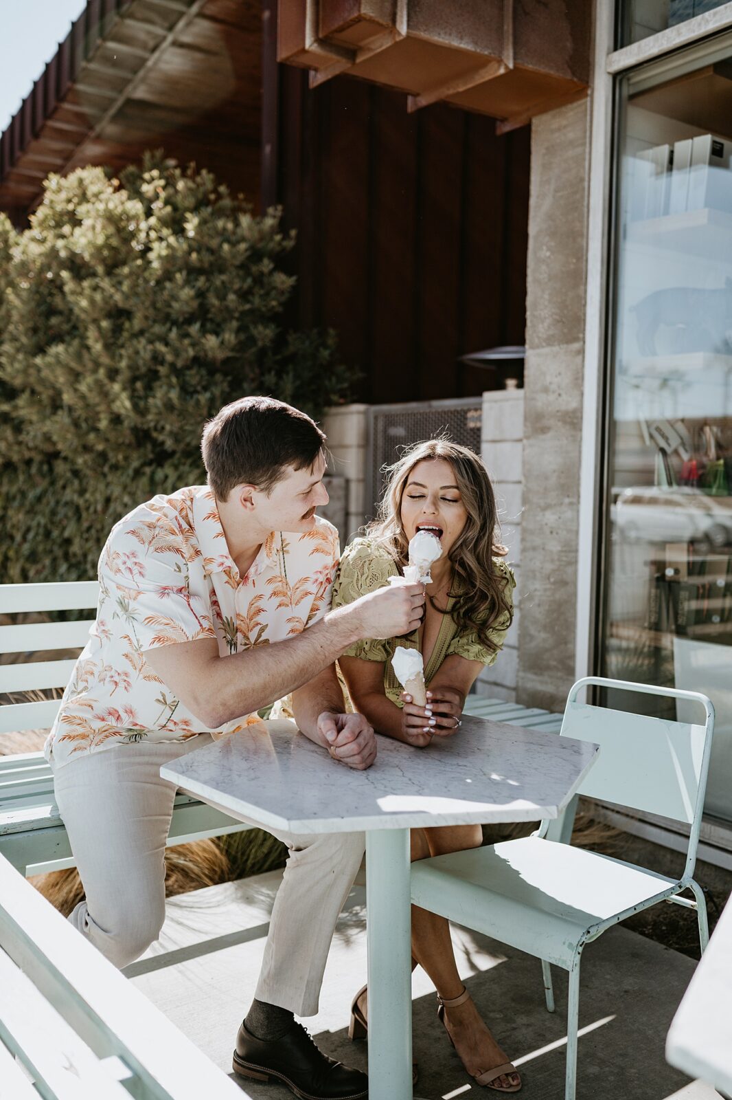 Couple sitting at a table outside with their ice cream, feeding one another