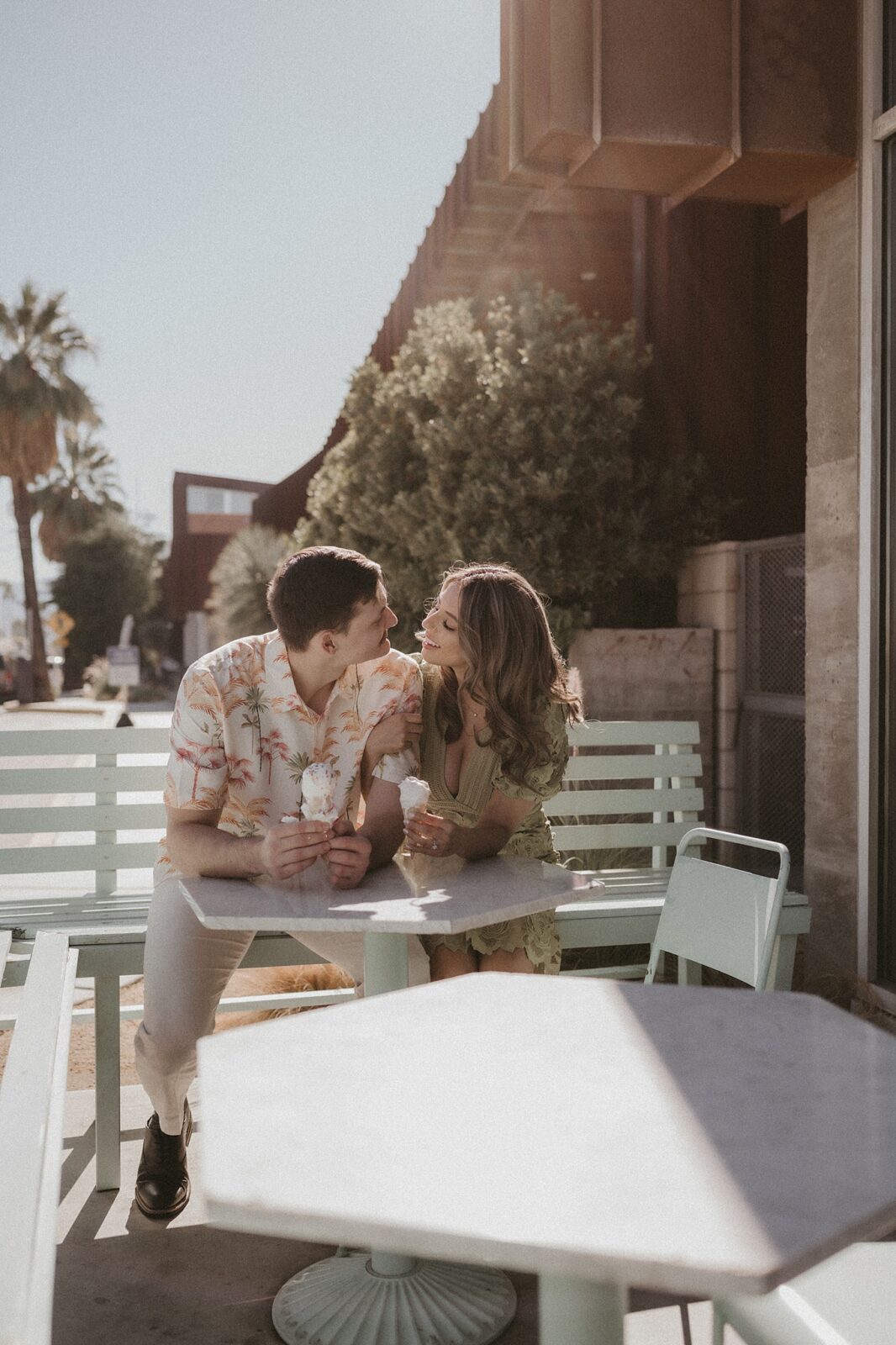 Couple cozied up at table outside of a shop, in downtown Palm Springs,  smiling at one another