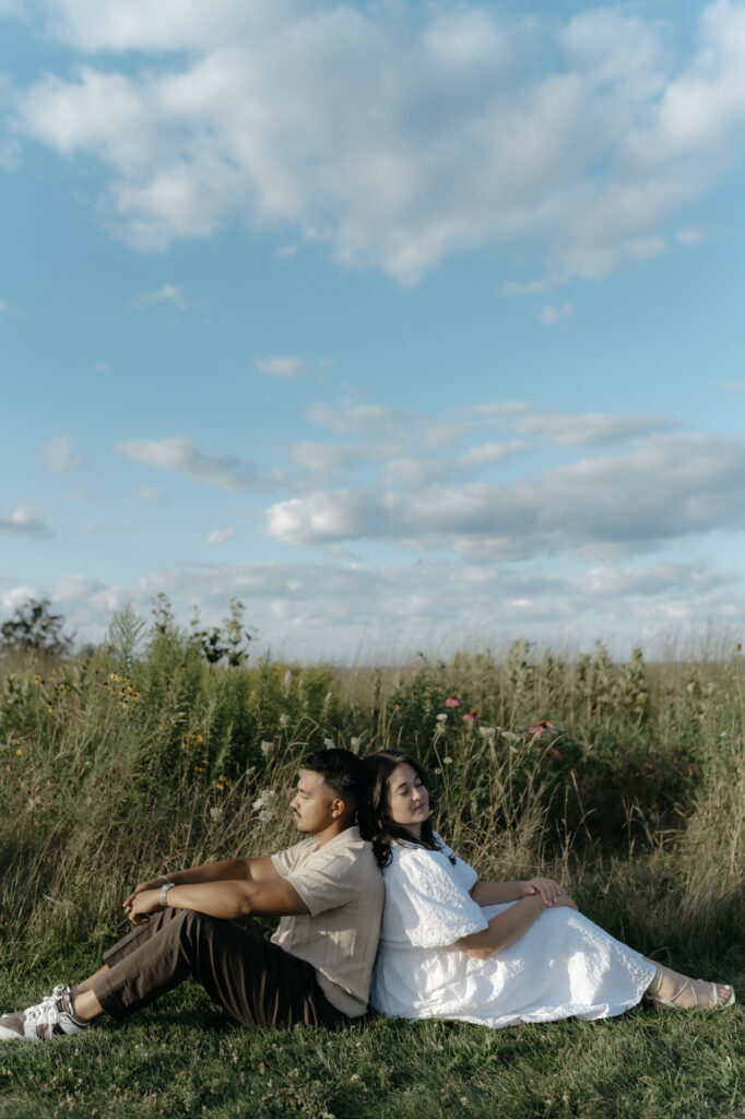 A couple sitting back-to-back in a field, capturing the quiet connection of authentic engagement photos.