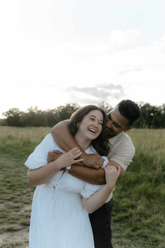 A joyful couple sharing a laugh during their authentic engagement photos in an open field.