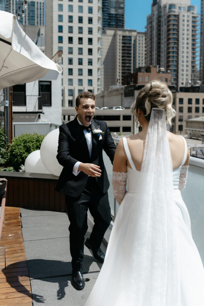 A groom reacts with a shocked, jaw-dropping expression during a private rooftop first look wedding photography reveal with his bride.