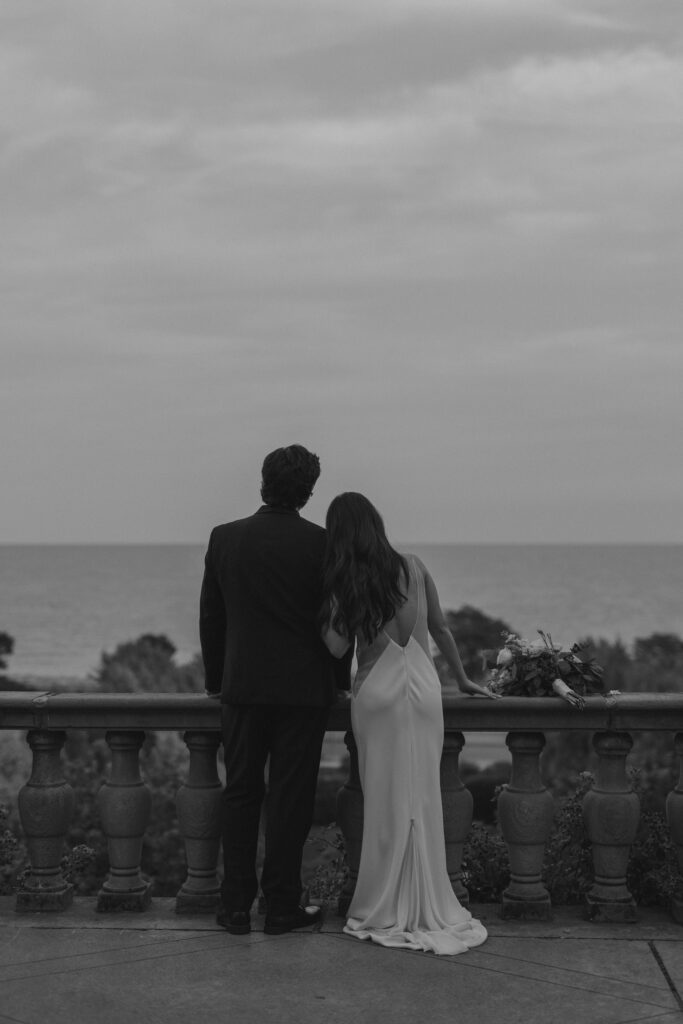 A cinematic black and white shot of a couple looking at the horizon, representing timeless monochrome wedding photography.