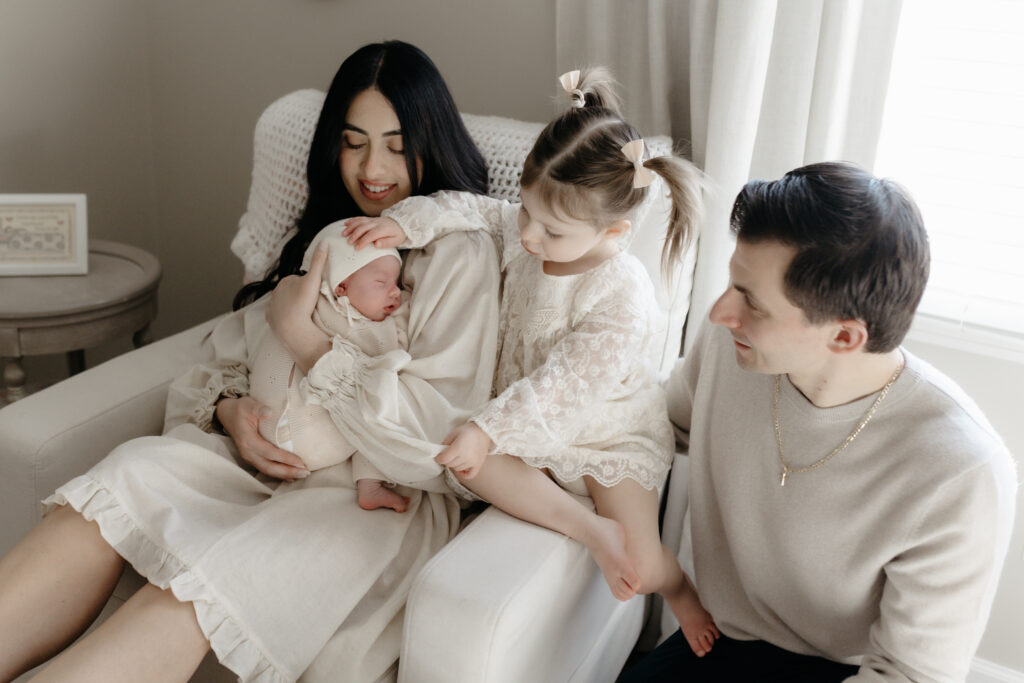 A toddler gently touching her newborn baby sibling during an in-home family newborn photography session with her parents.