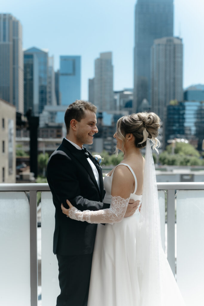 A bride and groom smile warmly at each other while embracing on a city balcony after their first look wedding photography reveal.
