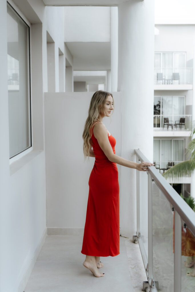 A female founder in a red dress standing on a modern balcony, demonstrating leadership routines to support a creative business vision.
