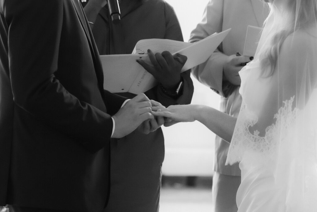 A black and white close-up of a couple exchanging rings while staying present during their wedding ceremony.