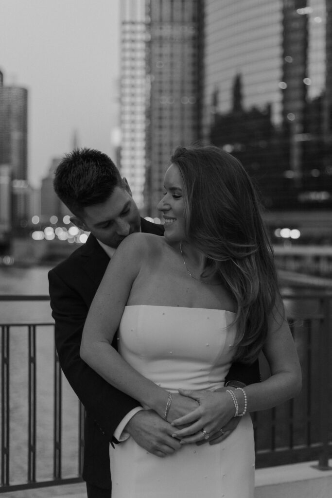A romantic black and white photograph of a groom embracing his bride from behind to capture cinematic wedding photos.