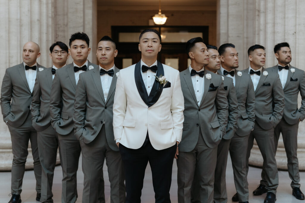 A groom in a white tuxedo jacket standing with groomsmen in slate gray suits.