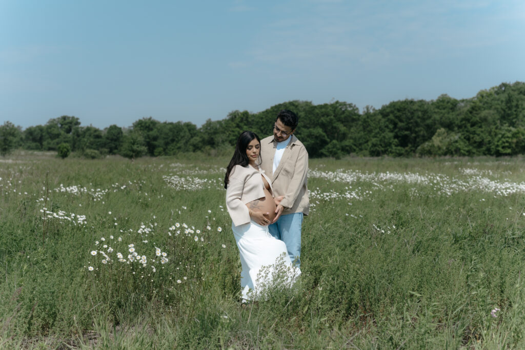 Maternity clothes for photoshoot selection shown by a couple holding a baby bump in a field of white daisies.