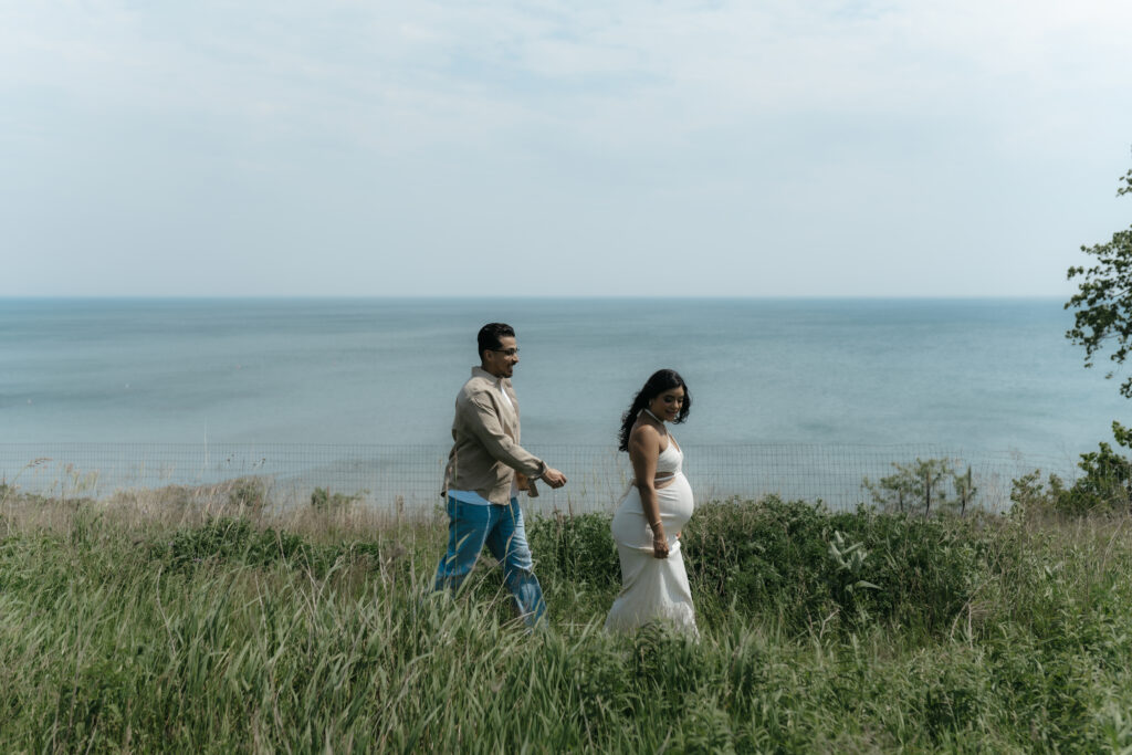 A man and pregnant woman walking on a cliff path wearing classic maternity clothes for photoshoot day.