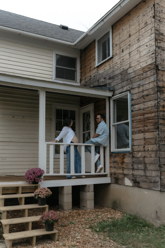 Expectant parents standing together on a rustic front porch during a relaxed lifestyle photoshoot.
