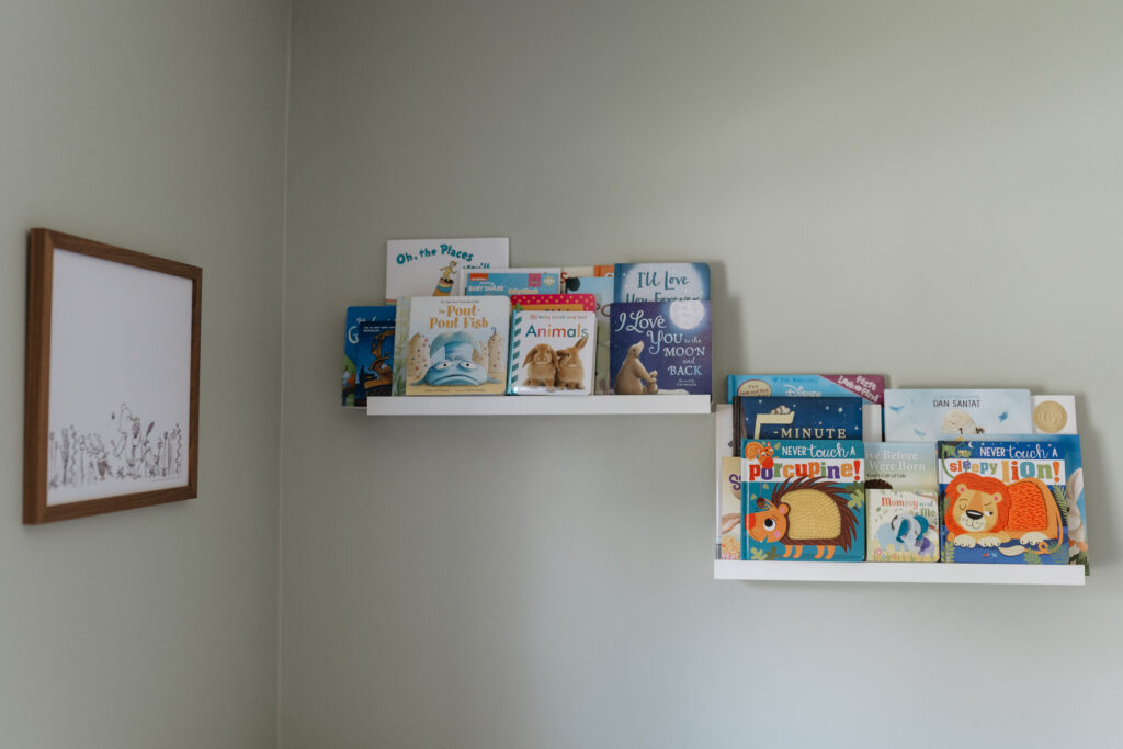 Colorful children books arranged beautifully on white floating shelves in a baby nursery.