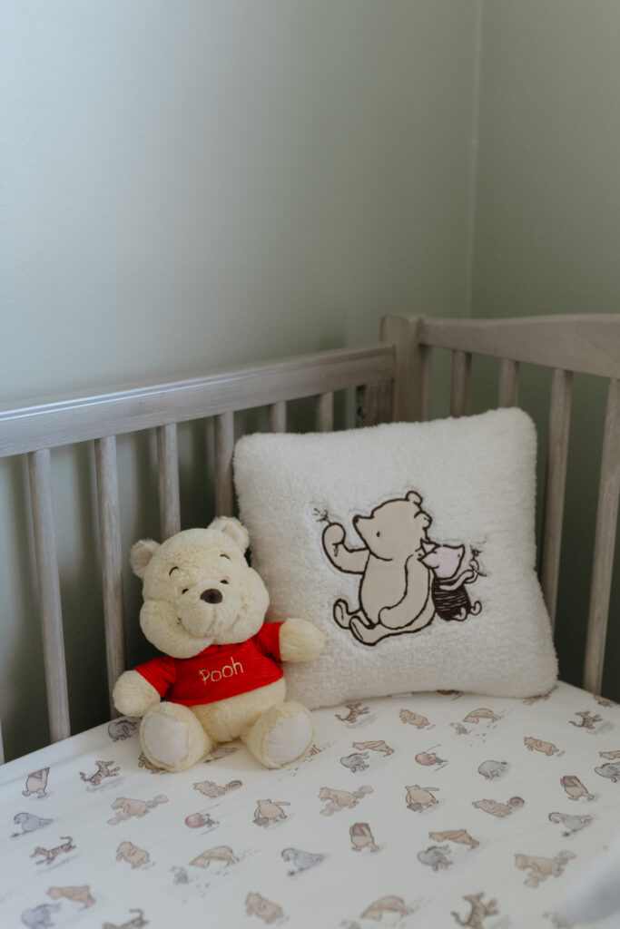 A classic Winnie the Pooh plush toy sitting on printed crib sheets next to a soft pillow.