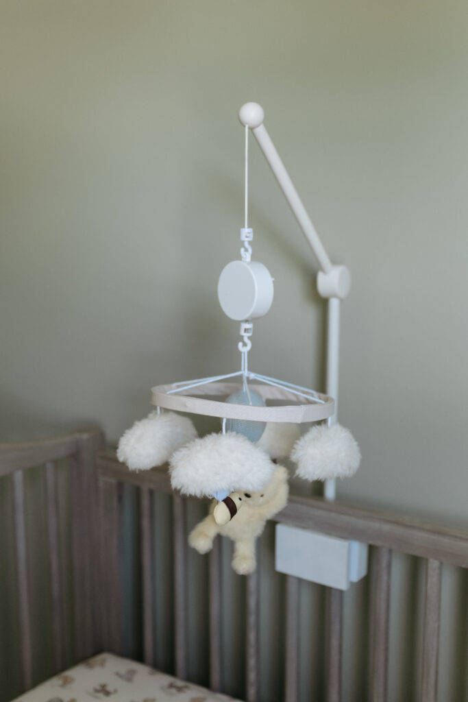 A simple white baby mobile with plush clouds hanging above a wooden crib.