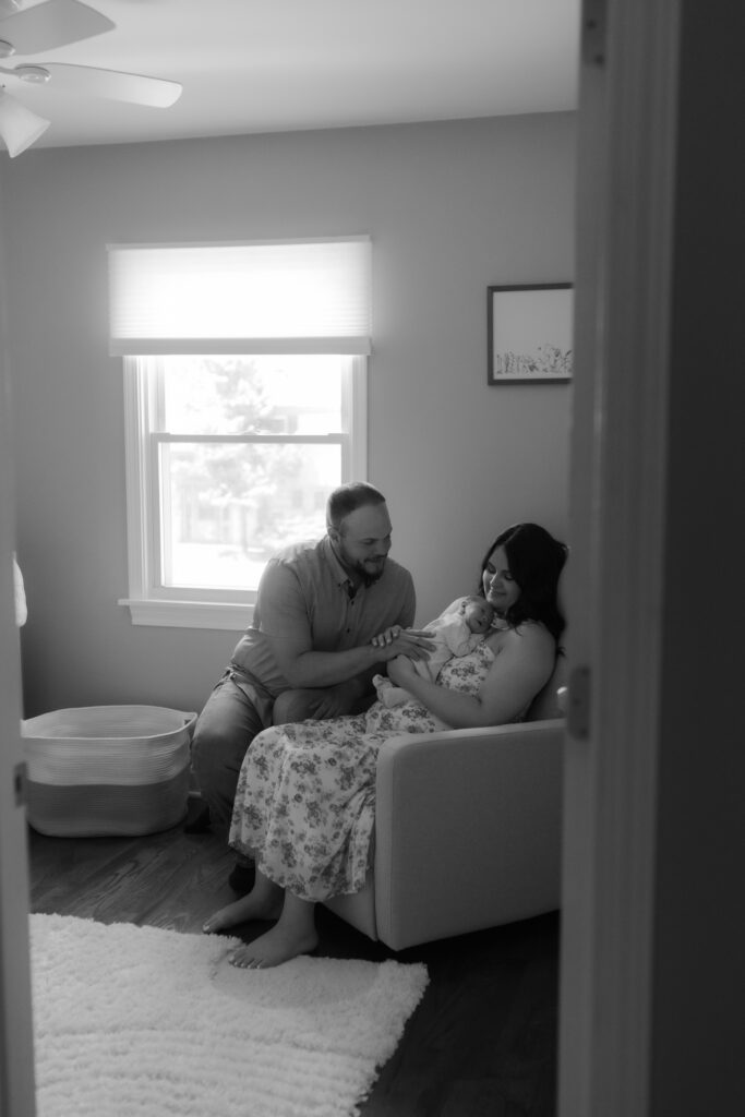A classic black and white portrait of a mother holding her baby in a chair while the father looks on.