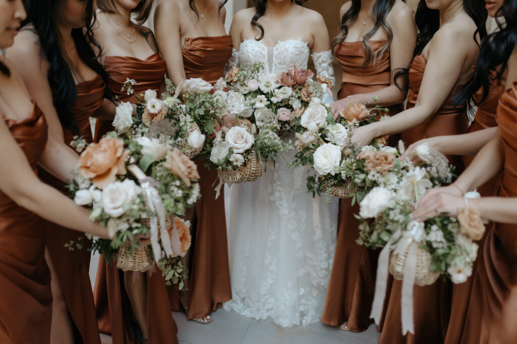 Bridesmaids in copper satin dresses holding unique woven flower baskets.