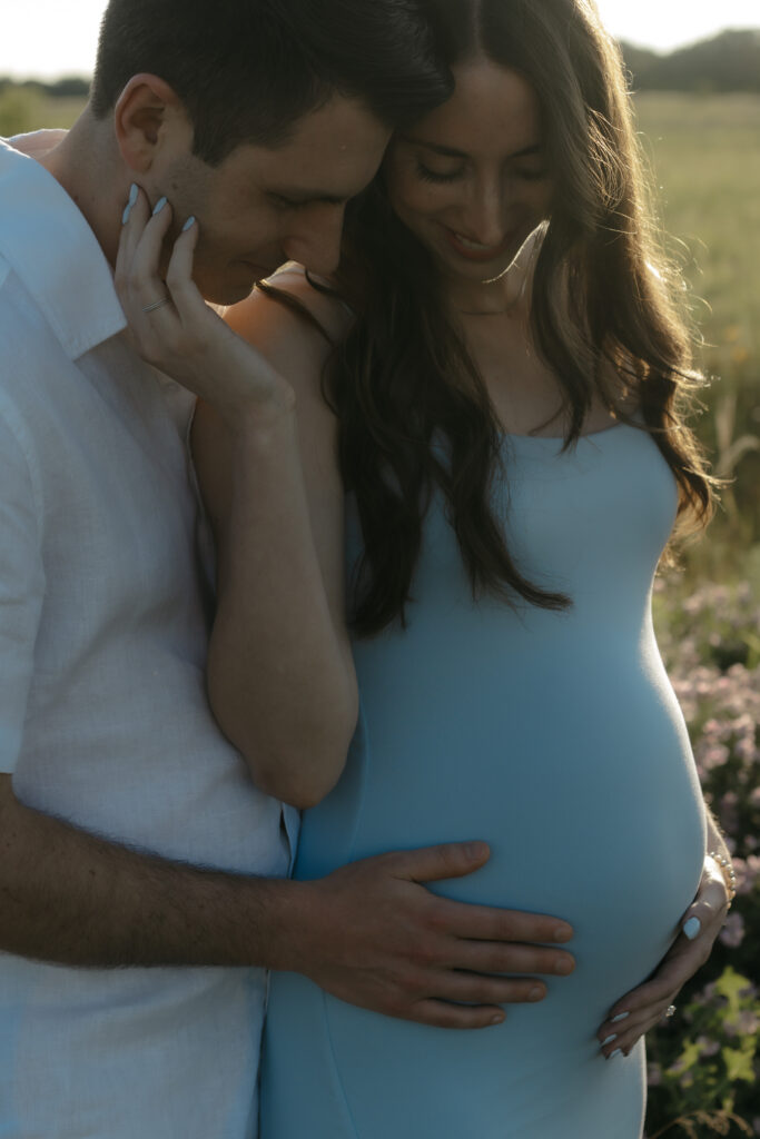 A close-up photograph of a groom holding his wife's face gently while looking down lovingly.