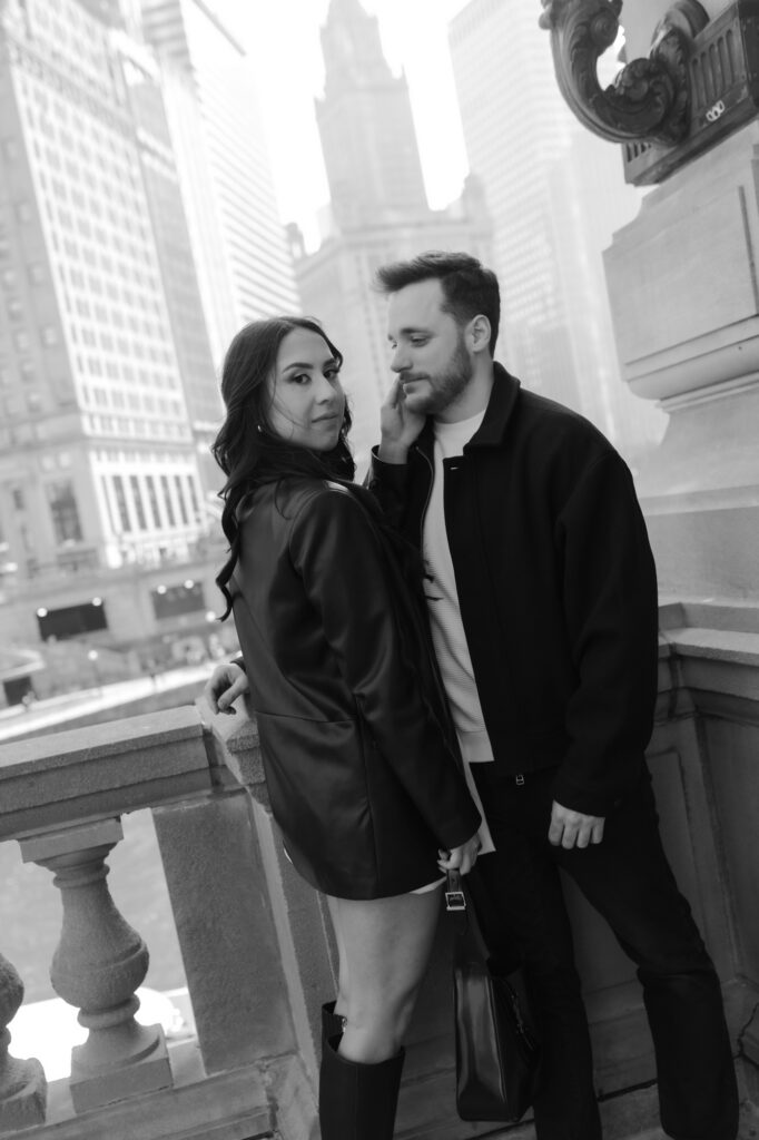 Black and white close up portrait of an elegant couple on a city bridge with high-rise skyscrapers blurred in the background.