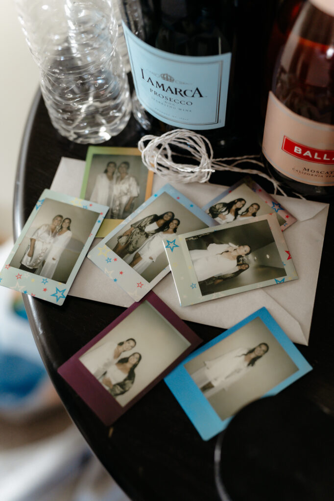 A collection of color polaroid photos of a bride and her bridesmaids placed on a table next to bottles of champagne.