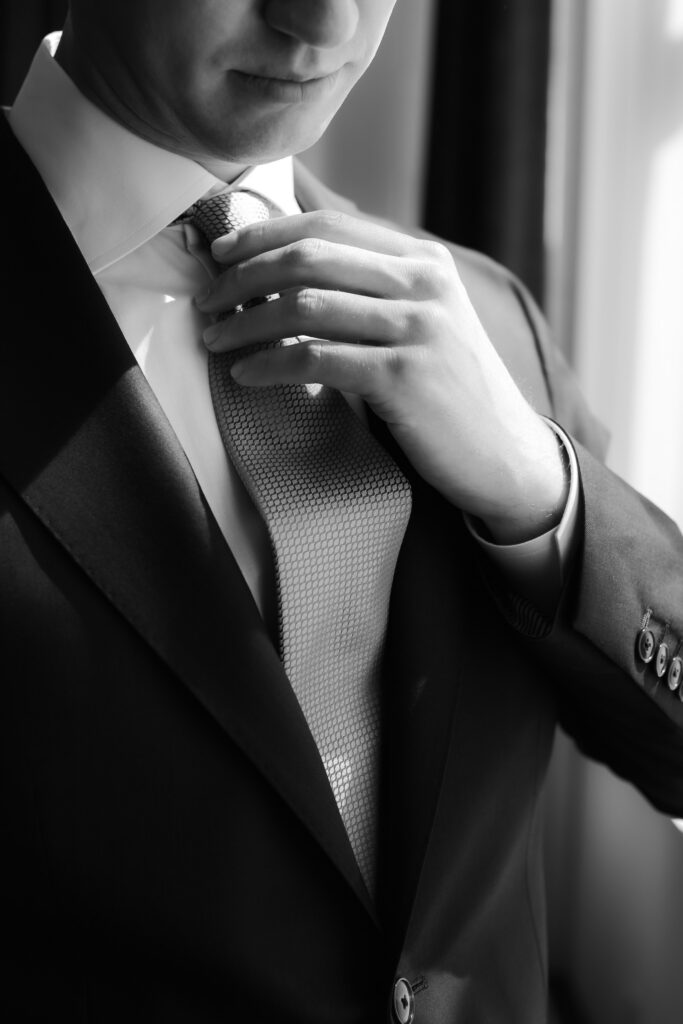 Close-up black and white detail shot of a groom adjusting his patterned wedding tie.