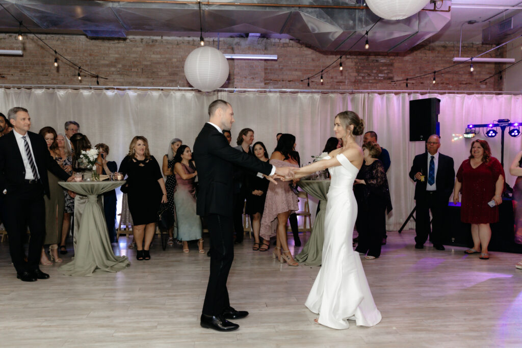 Newlyweds enjoying their first dance surrounded by cheering guests under paper lanterns.
