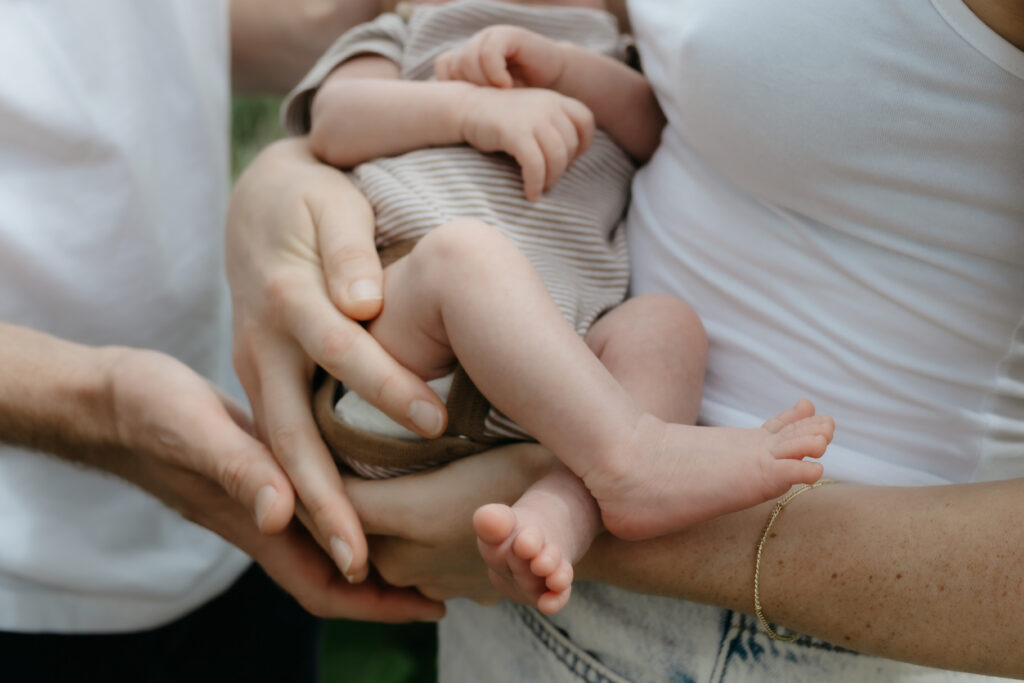 Close up shot of parents holding their newborn baby showing tiny bare feet and hands.