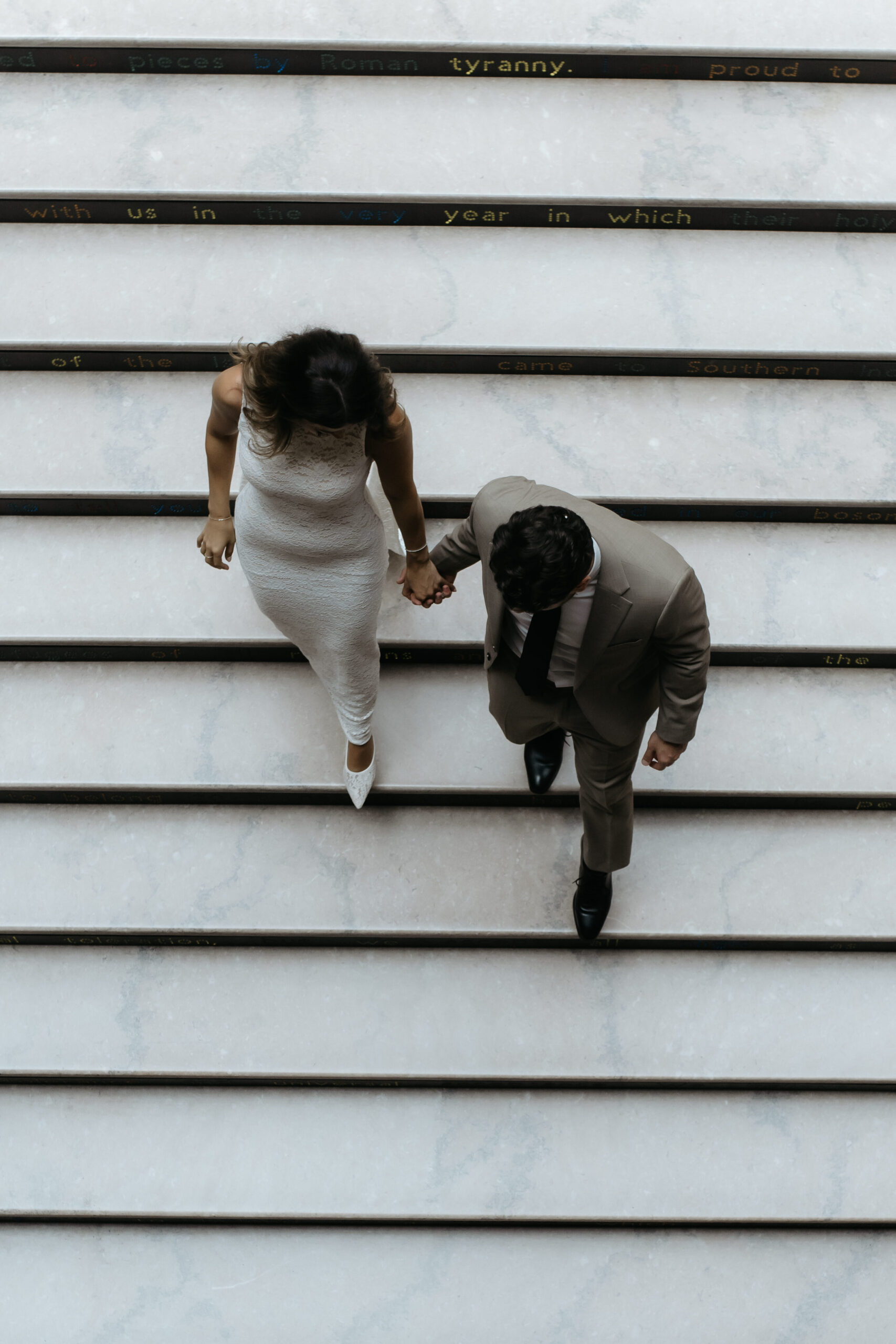 Directly overhead view of a couple holding hands while walking down wide marble museum stairs.
