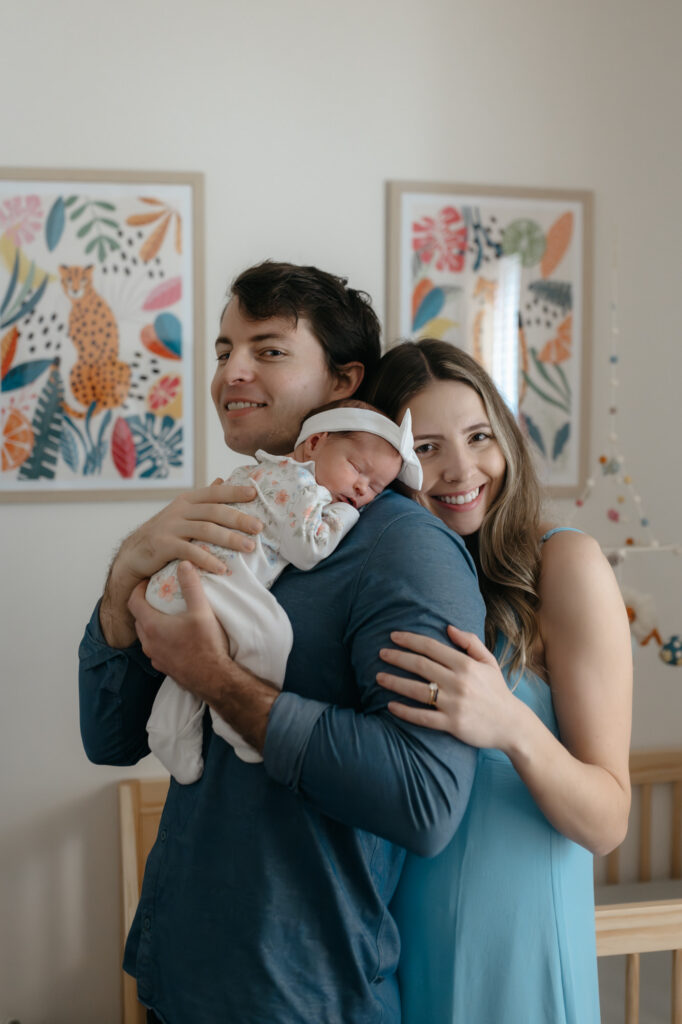 Happy parents smiling together while holding their sleeping baby girl in front of colorful nursery art.