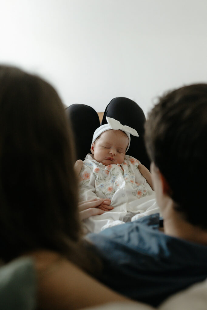 Over-the-shoulder view of parents looking down at their sleeping newborn baby resting in their lap.