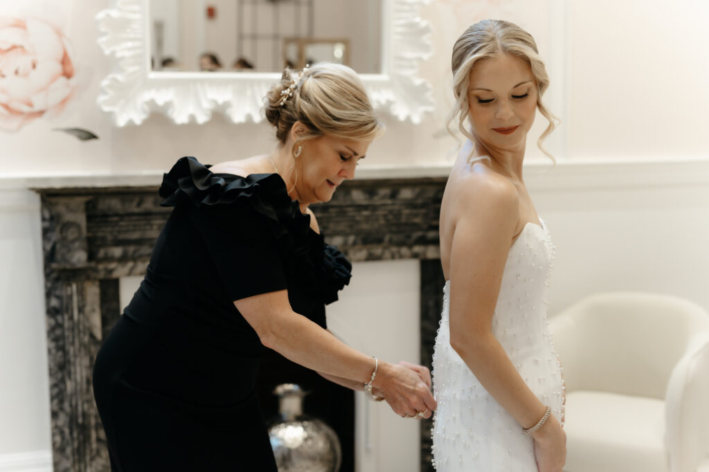 Helping the bride button up the back of her white strapless wedding gown.