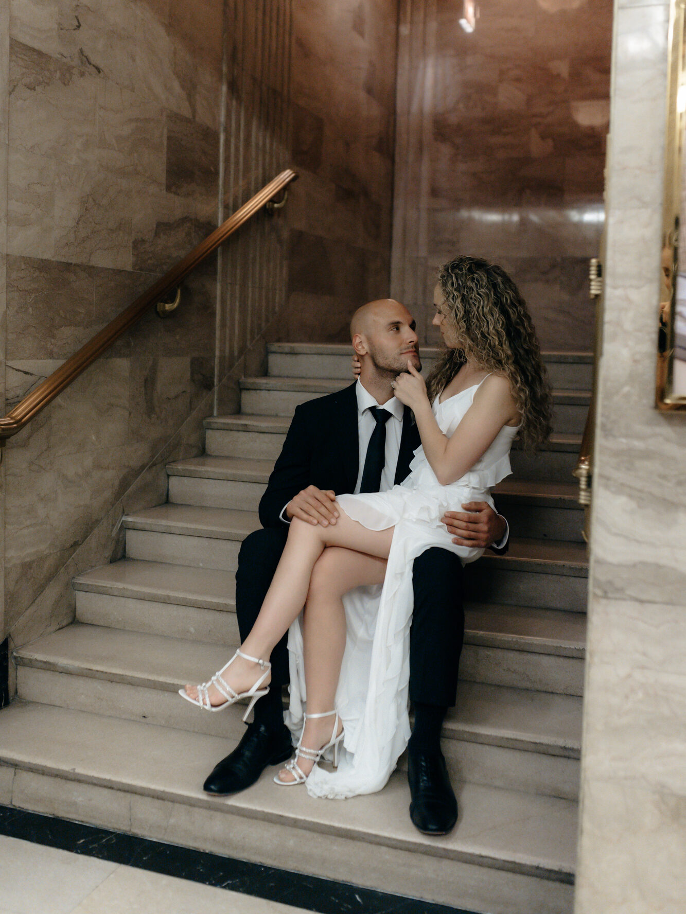 A groom holding his bride on a grand marble staircase inside a luxury historic venue.