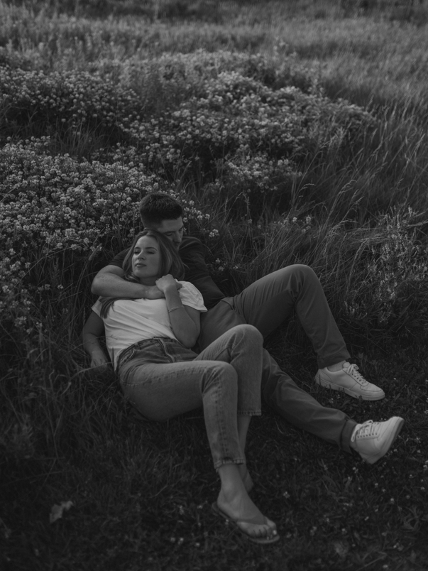 Black and white photo of a couple lying down together in a field of wildflowers.