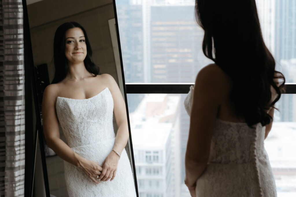 Reflection of a bride in a full length mirror smiling while wearing her wedding dress.