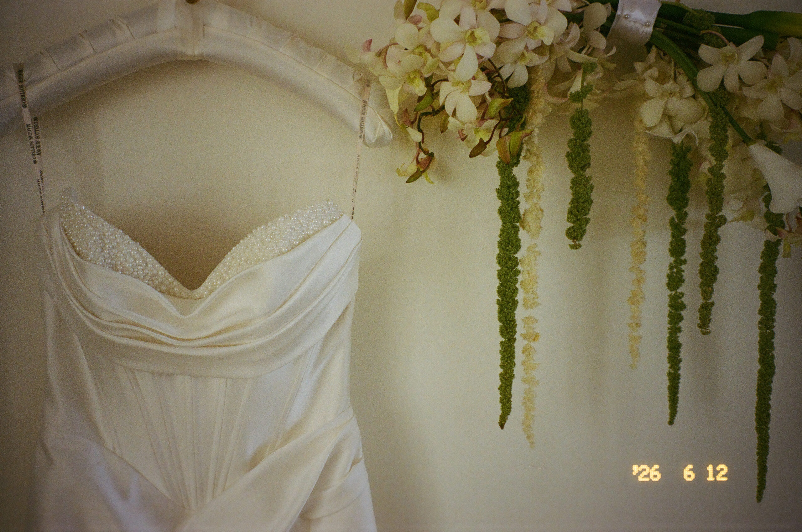 White wedding dress with beaded corset hanging next to a floral arrangement captured on 35mm film.